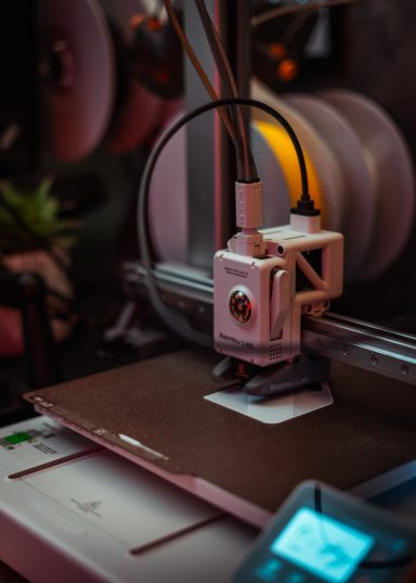 Close-up of a 3D printer's extruder and build plate in a dimly lit workspace.