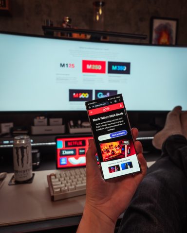 A person holding a smartphone displaying streaming service options in a cosy room.